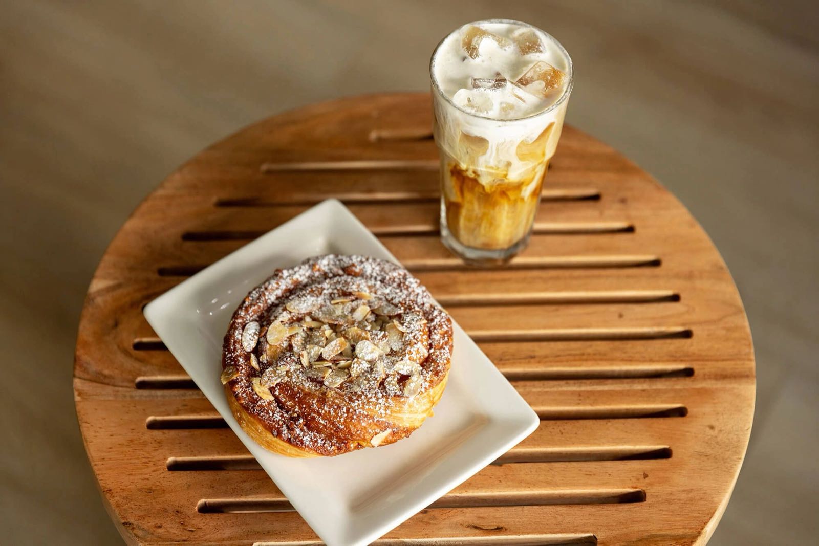 Iced coffee and an almond pastry on a wooden table at Sobar